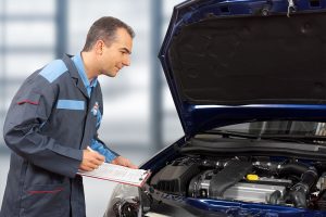 Mann in BOSCH Outfit, der auf ein Klemmbrett etwas aufschreibt. Neben ihm eine geöffnete Motorhaube
